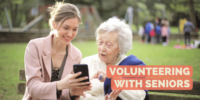 A young woman sits on a park bench with a senior citizen and shows her something on a smartphone